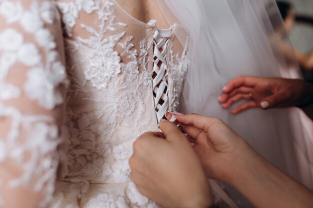 Las manos de las damas de honor están atando el corsé del vestido de novia