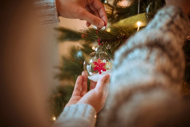 Manos decorando arbol de navidad con adornos.