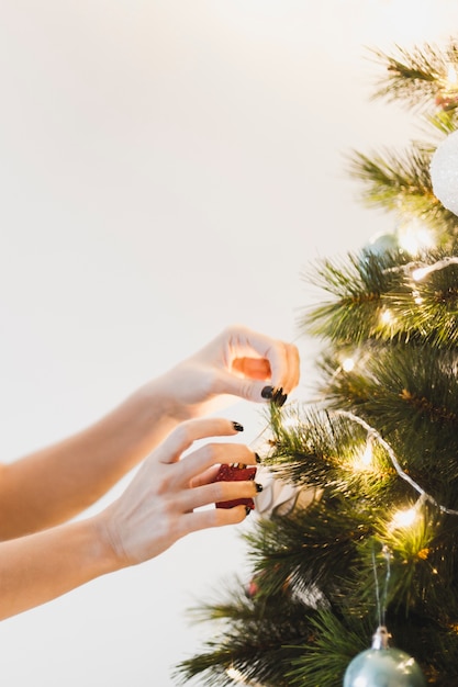 Manos decorando árbol de navidad iluminado