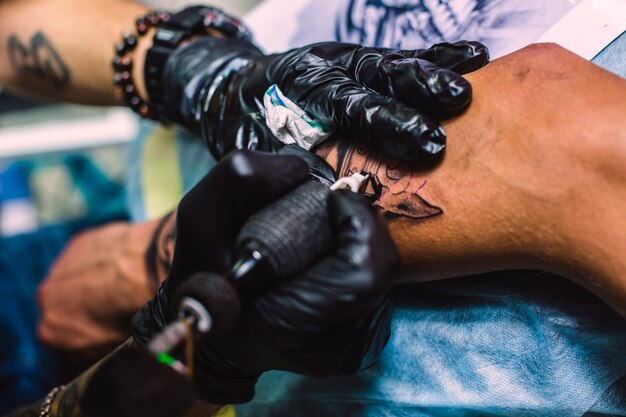 Manos dibujando tatuajes en el brazo con la máquina de la aguja