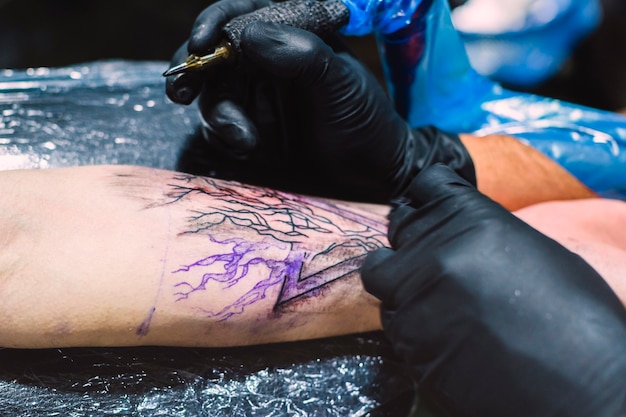 Manos dibujando tatuajes con la máquina en el brazo