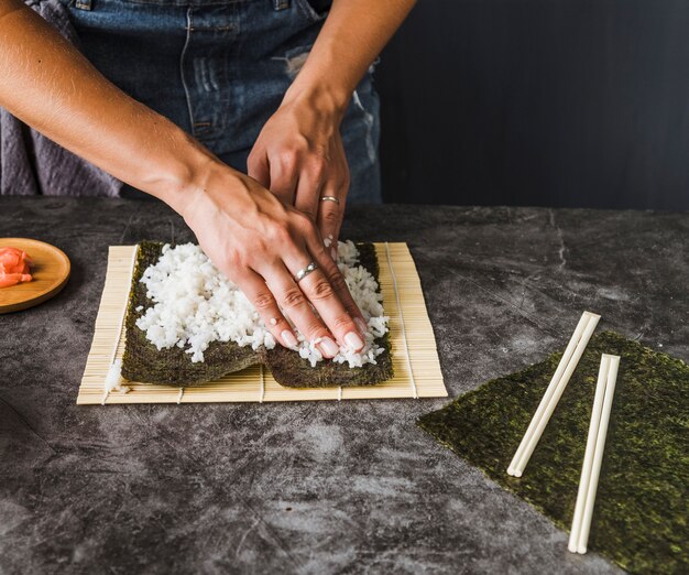 Manos dividiendo el arroz de manera uniforme en nori