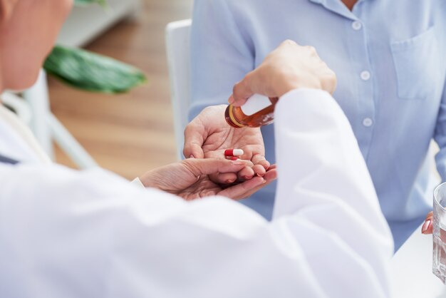 Manos de doctora irreconocible dando píldoras al paciente