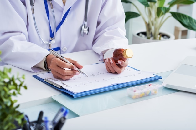 Manos de doctora mirando cardiograma y sosteniendo la botella de medicina