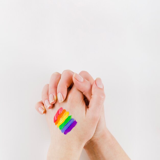 Manos entrelazadas con una bandera del orgullo lgbt pintada