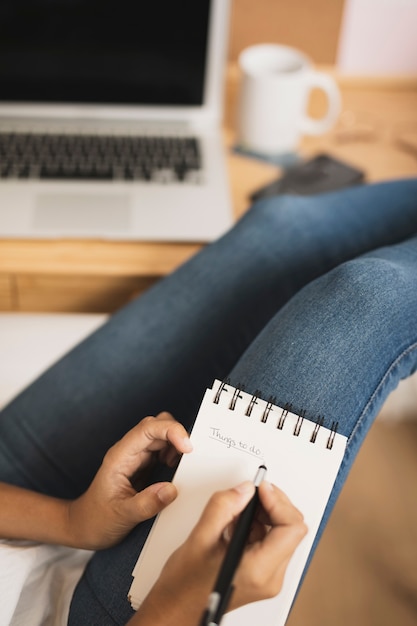 Manos escribiendo en el cuaderno junto a una computadora portátil