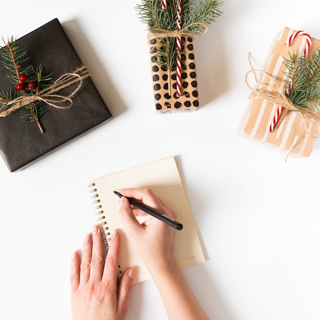 Manos escribiendo en cuaderno con regalos envueltos alrededor