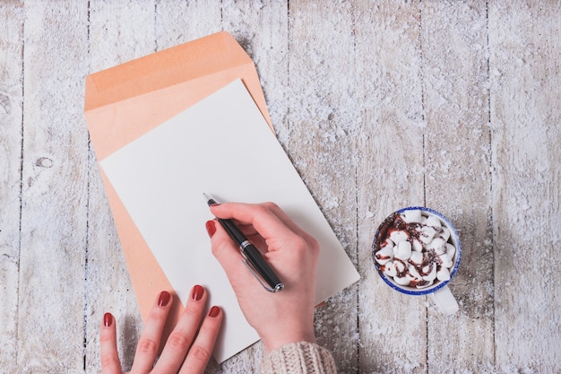 Manos escribiendo en un papel con una taza al lado