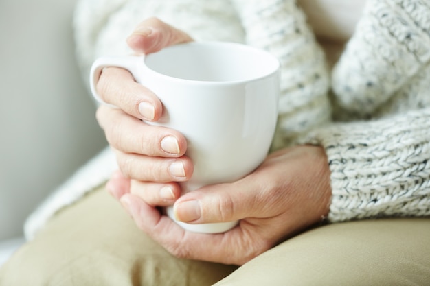 Manos femeninas arrugadas que sostienen la taza de café