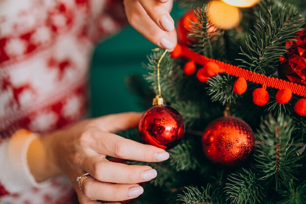 Manos femeninas de cerca, decorando el árbol de navidad con bolas rojas