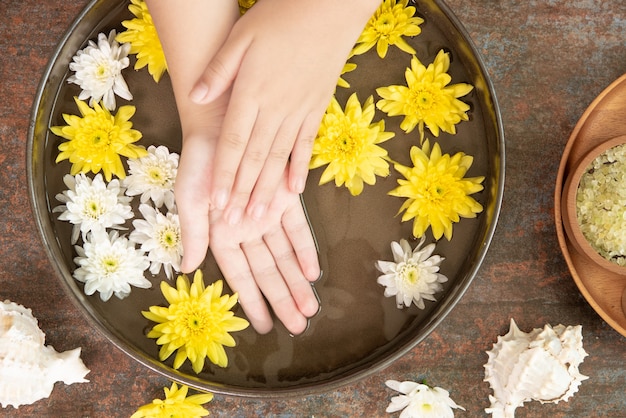 Manos femeninas y cuenco de agua de spa con flores, de cerca. Manos Spa.