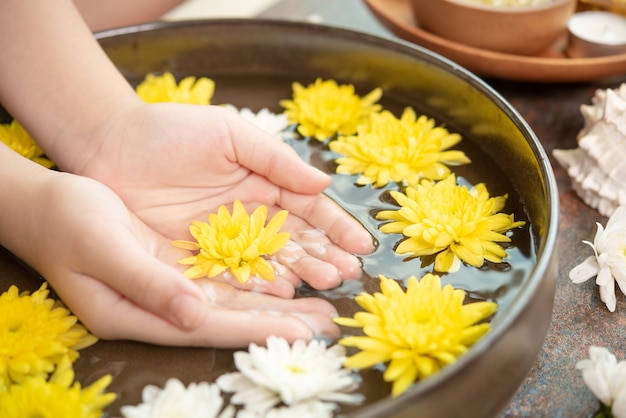 Manos femeninas y cuenco de agua de spa con flores, de cerca. Manos Spa.