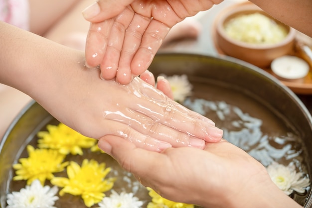 Manos femeninas y cuenco de agua de spa con flores, de cerca. Manos Spa.