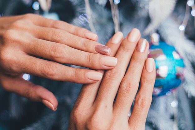 Manos femeninas con diseño de uñas de año nuevo de Navidad. Manicura de esmalte de uñas beige nude, un dedo bronce dorado brillante