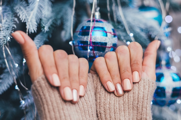 Manos femeninas con diseño de uñas de año nuevo de Navidad. Manicura de esmalte de uñas beige nude, un dedo bronce dorado brillante