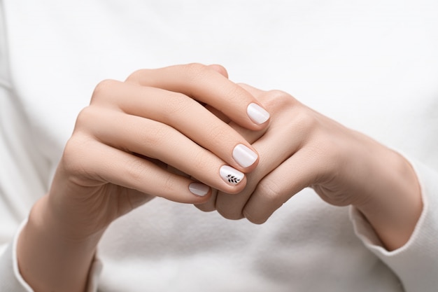 Manos femeninas con diseño de uñas blanco, de cerca.