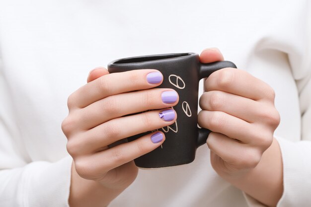 Manos femeninas con diseño de uñas púrpura con taza negra.