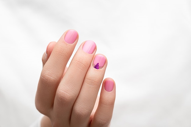 Manos femeninas con diseño de uñas rosa sobre fondo de tela blanca.