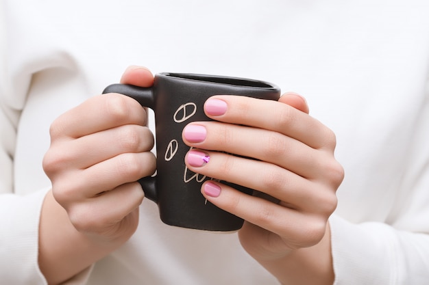 Manos femeninas con diseño de uñas rosa sosteniendo la taza negra.