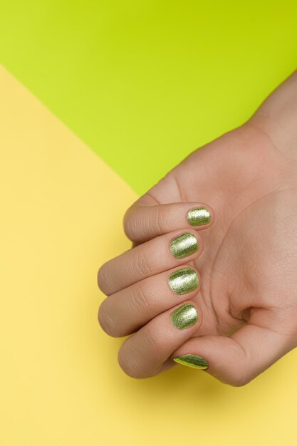 Manos femeninas con diseño de uñas verde. Manos cuidadas de esmalte de uñas verde. Manos femeninas sobre fondo verde