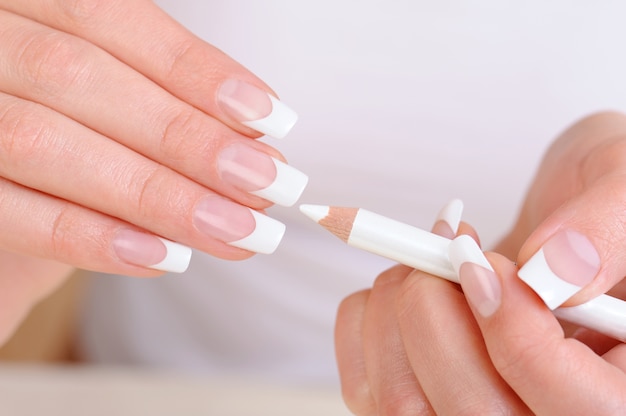 Manos femeninas con un lápiz de manicura blanco