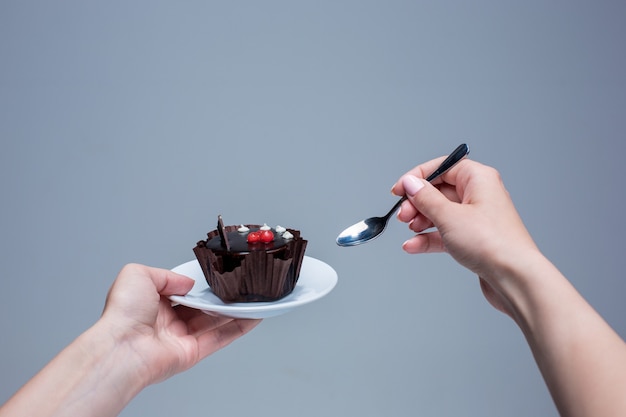 Manos femeninas manteniendo la torta con cuchara sobre fondo gris