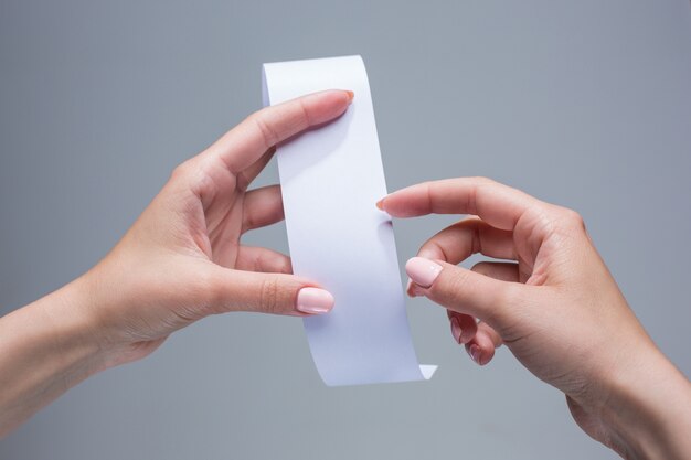 Manos femeninas con papel de transacción vacío o cheque en papel sobre fondo gris
