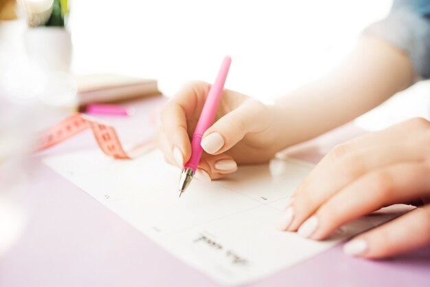 Manos femeninas con pluma. Escritorio rosa de moda.