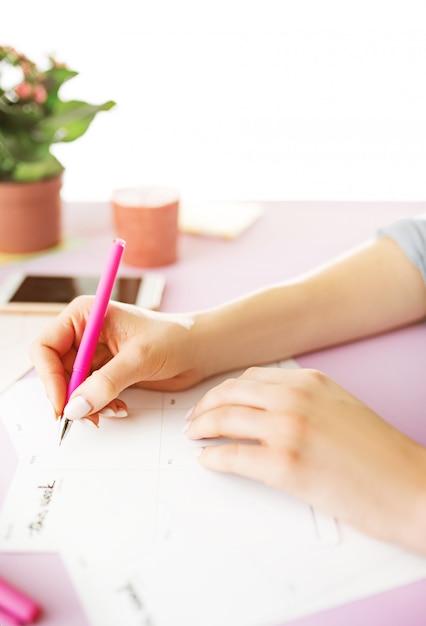 Manos femeninas con pluma. teléfono en el moderno escritorio rosa.