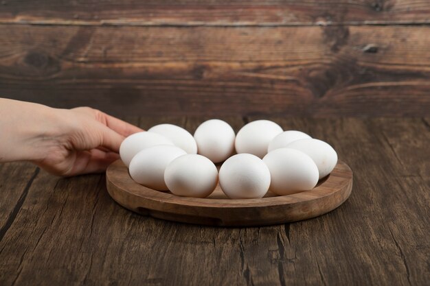 Manos femeninas que sostienen la tabla de madera con huevos crudos en la superficie de madera.