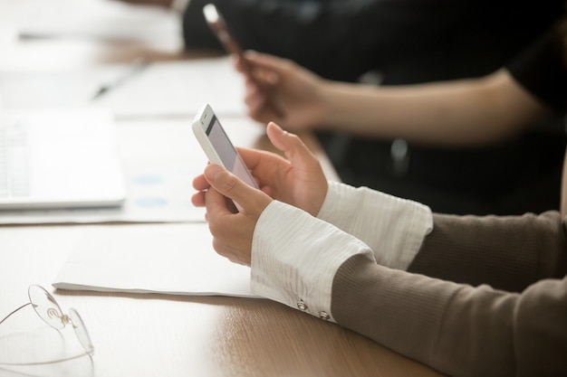 Manos femeninas que sostienen el teléfono móvil en la reunión de la oficina, opinión del primer