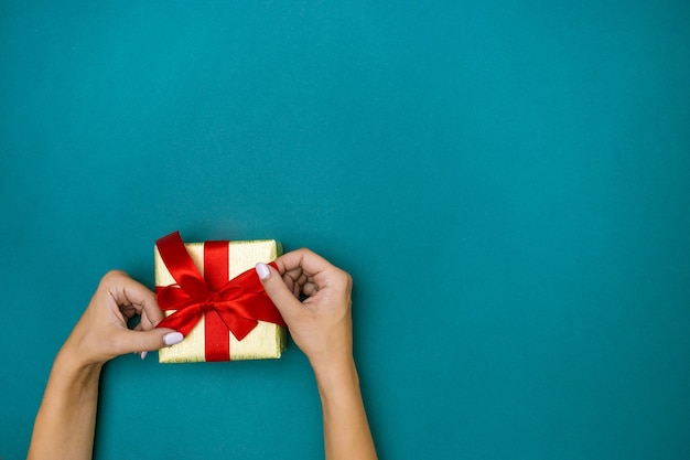 Las manos femeninas con regalo sobre fondo azul.