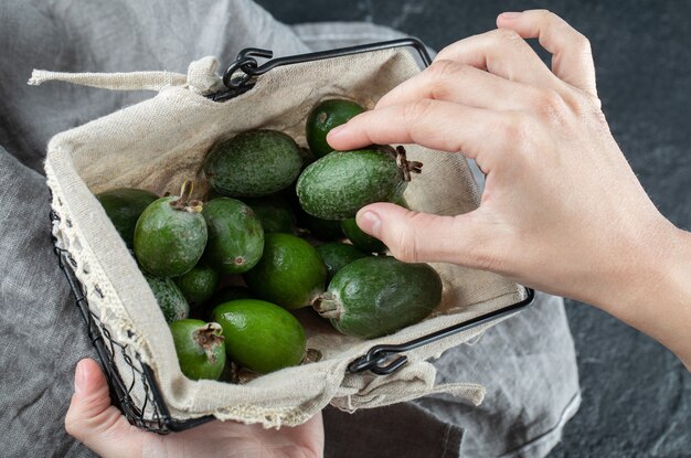 Manos femeninas sacando fruta feijoa de la cesta.