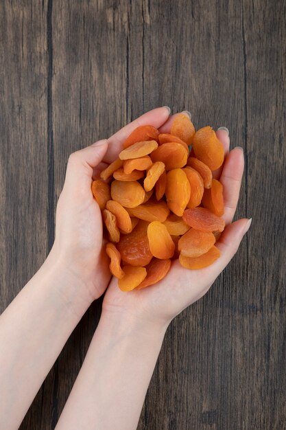 Manos femeninas sosteniendo un montón de frutos secos saludables de albaricoque en una mesa de madera.