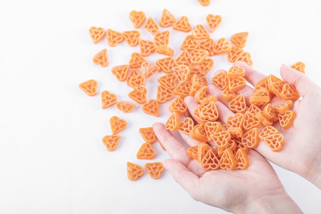 Manos femeninas sosteniendo un montón de pasta cruda en forma de corazón en blanco.