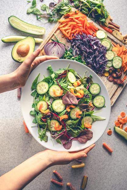 Foto gratuita manos femeninas sosteniendo un plato de ensalada vegana con verduras frescas vista superior