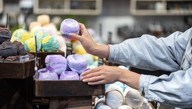 Manos femeninas sostienen bombas de baño brillantes en una tienda de cosméticos. Concepto de cuidado corporal.