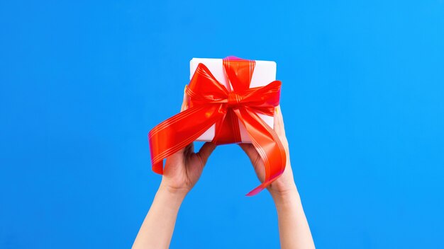 Manos femeninas sostienen una caja de regalo con cinta roja