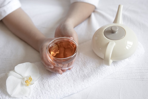 Las manos femeninas sostienen una taza de té, una flor de orquídea y una tetera, el concepto de tratamientos de spa y relajación.