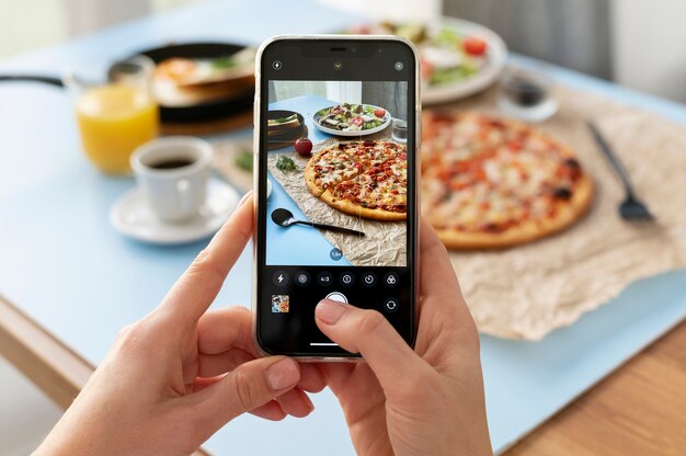 Manos femeninas tomando fotos de pizza en rodajas y plato de ensalada