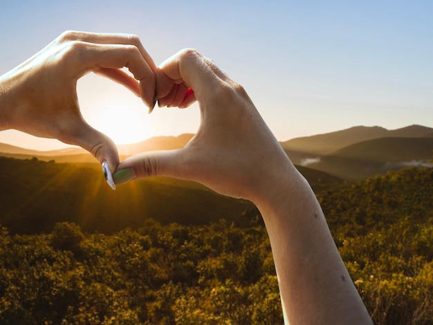 Manos en forma de corazón en una puesta de sol