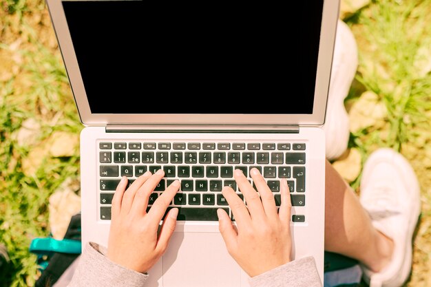 Manos de freelancer escribiendo en la computadora portátil en la naturaleza en un día soleado