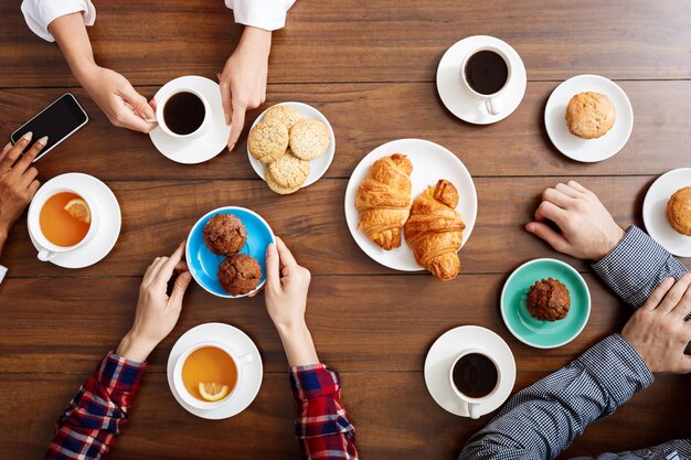 Las manos de la gente en la mesa de madera con cruasanes y café.