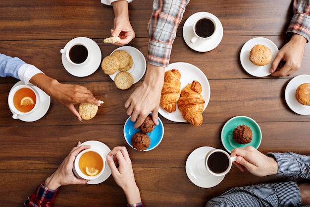 manos de la gente en la mesa de madera con cruasanes y café.