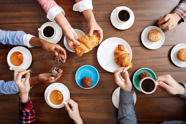 manos de la gente en la mesa de madera con cruasanes y café.