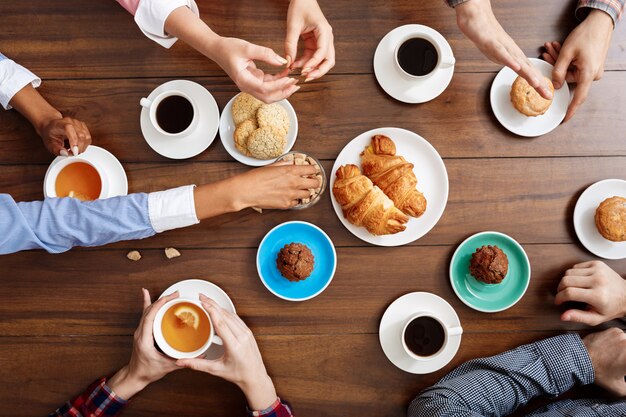 manos de la gente en la mesa de madera con cruasanes y café.