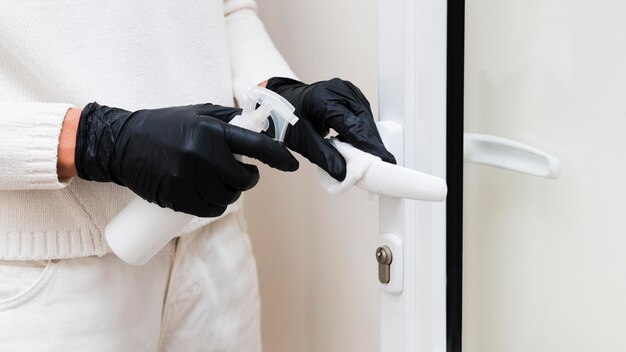 Manos con guantes desinfectando la manija de la puerta