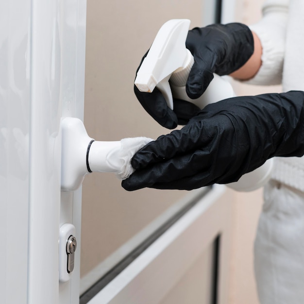 Manos con guantes desinfectando la manija de la puerta