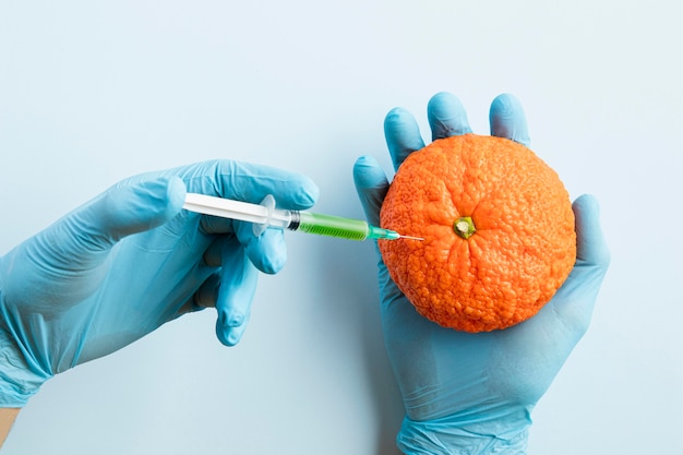 Manos con guantes e inyectando productos químicos en una naranja