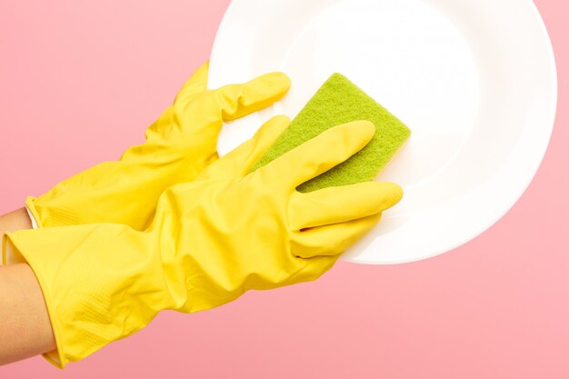 Manos en guantes protectores amarillos lavando un plato